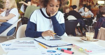 young-african-woman-entrepreneur-with-serious-concentrated-expression-sitting-coworking-cafe-with-touch-pad-pc-papers-analyzing-financial-information-tablet-resting-elbow-table_273609-5554